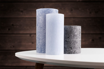 Blue and gray candles on a white shiny table against a dark chestnut brown timber background.