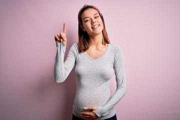 Young beautiful teenager girl pregnant expecting baby over isolated pink background pointing finger up with successful idea. Exited and happy. Number one.