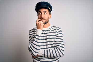 Young handsome sailor man with beard wearing navy striped uniform and captain hat with hand on chin...