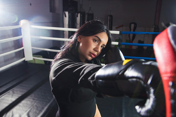 A beautiful girl in boxing gloves hits her paws in the ring. Sexy woman is training in the gym....