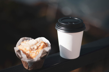 Coffee in a disposable white glass with a black lid and a delicious cupcake.