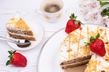 Cake with cream and nuts on a white plate, juicy strawberries and a cup of coffee and flowers on a white shabby table.