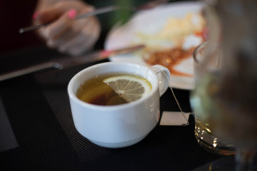 Black tea with lemon in a white mug on the table.