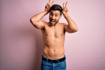 Young handsome strong man with beard shirtless standing over isolated pink background Posing funny and crazy with fingers on head as bunny ears, smiling cheerful