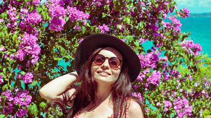 Girl in the flowers in the summer. Woman in a hat on a background of pink plants. The concept of natural beauty and youth. Natural emotions of joy. Copy space