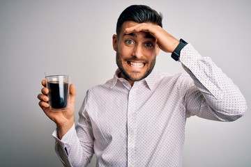 Young handsome man drinking a cup of hot coffee over white isolated background stressed with hand on head, shocked with shame and surprise face, angry and frustrated. Fear and upset for mistake.