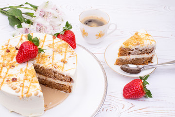 Cake with cream and nuts on a white plate, juicy strawberries and a cup of coffee and flowers on a white shabby table.