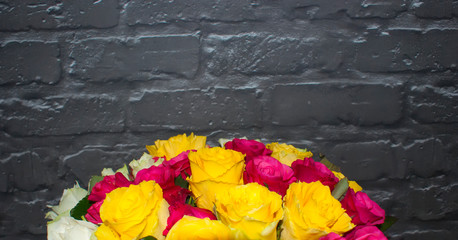 A bouquet of bright roses on a background of black brick wall. White, pink and yellow roses in one bouquet.
