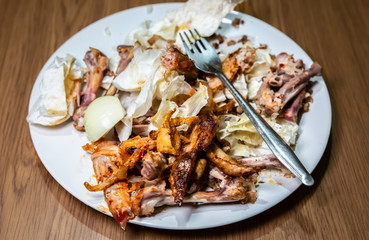 Leftovers on the big plate. Waste of food. Chicken bones and some vegetables left after lunch.