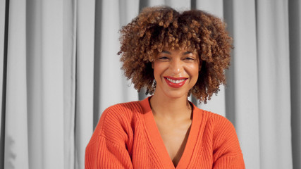 Closeup portrait of laughing mixed race black woman with textured curly afro hair in bright orange...
