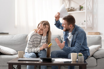 Angry husband shouting at his guilty wife with huge credit card bills at home