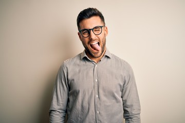 Young handsome man wearing elegant shirt and glasses over isolated white background sticking tongue out happy with funny expression. Emotion concept.