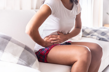 Woman sitting on a couch at home holding her appendix in a stomach ache