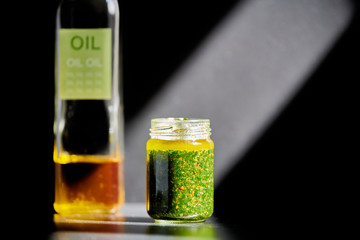 The Wild green garlic pesto jar on focus and the olive oil bottle under the reflected light of the sun on a black background