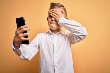 Young little caucasian kid using smartphone and looking at the screen of the phone stressed with hand on head, shocked with shame and surprise face, angry and frustrated. Fear and upset for mistake.