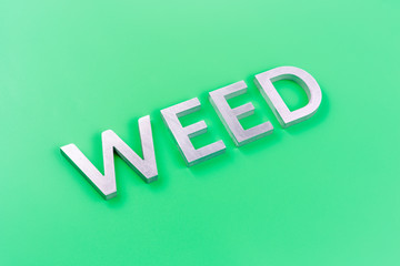 the word weed laid with silver metal letters on pastel green background with diagonal perspective