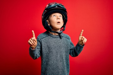 Young little caucasian kid wearing vintage biker motorcycle helmet and googles over red background...