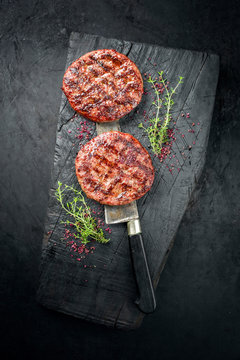 Barbecue Wagyu Hamburger with red wine salt and herbs as top view on a charred wooden board