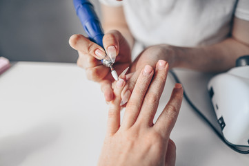 Hardware professional manicure process, cleaning of nails by a milling cutter. Close up female hands in beauty salon. Finger nail treatment, making process. Electric nail file drill in action