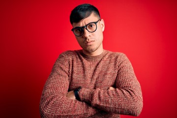 Young handsome hispanic man wearing nerd glasses over red background skeptic and nervous,...