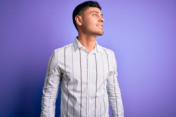 Fototapeta premium Young handsome hispanic man wearing elegant business shirt standing over purple background looking away to side with smile on face, natural expression. Laughing confident.