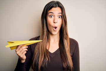 Young beautiful girl holding paper plane standing over isolated white background scared in shock with a surprise face, afraid and excited with fear expression