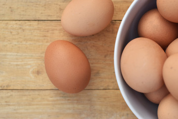 Brown chicken eggs in a white bowl on wooden table soft focus.