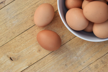 Brown chicken eggs in a white bowl on wooden table soft focus.