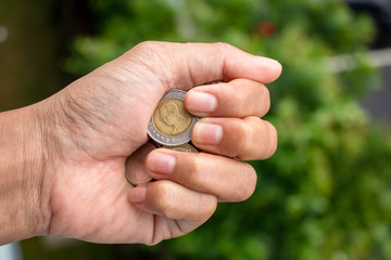 Clutch a coin to save money. The economy was bad during the epidemic. holding the coins on natural background. in saving money concept. copy space