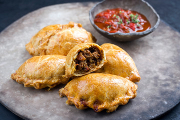 Traditional South American empanada de carne offered with a chili dip as closeup on a rustic modern design plate