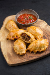 Traditional South American empanada de carne offered with a chili dip as closeup on a rustic wooden board