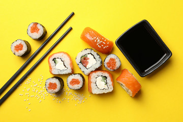 Sushi rolls, chopsticks and soy on yellow background, top view