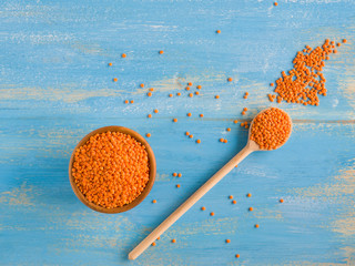 Red or Canadian Orange Lentil on wooden bowl and spoon on blue background. Vegetarian diet. Source...