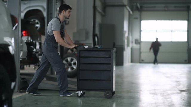 A young automaker pushes a box of tools in the workshop.
