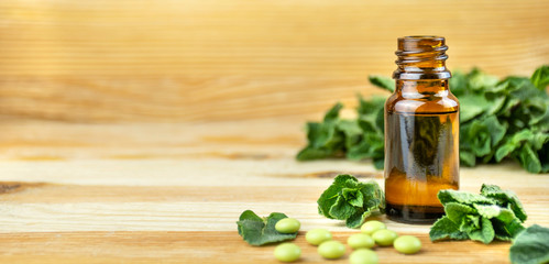 Peppermint oil in a glass bottle with fresh mint leaves on a wooden table. Copy space.