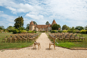 Wedding ceremony on the background of old castle. Rows of wooden chairs for guests standing on the grass in garden of France chateau. Beautiful area for open-air celebration