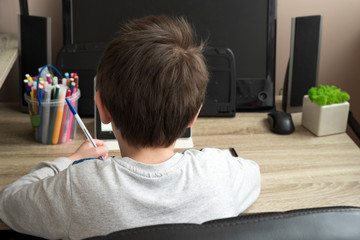 Boy studying at home with tablet and doing school homework. Distance learning online education or stay at home concept. Soft focus. Back view