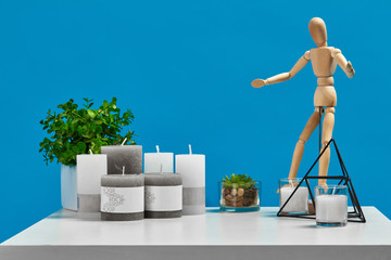 White table with green flower and succulent in pot, wooden figurine of human, some candles with...