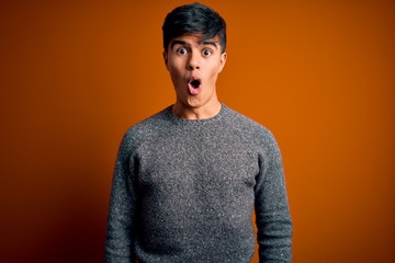 Young handsome man wearing casual sweater standing over isolated orange background afraid and shocked with surprise and amazed expression, fear and excited face.