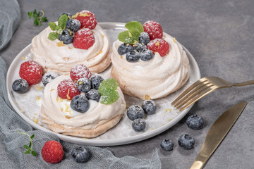 Mini pavlova meringue cakes with fresh raspberries and blueberries with mint leaves.