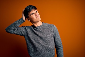 Young handsome man wearing casual sweater standing over isolated orange background confuse and wondering about question. Uncertain with doubt, thinking with hand on head. Pensive concept.