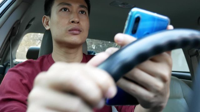Man Using Smartphone Behind Steering Wheel – Driving Safety and Mobile Technology Concept
