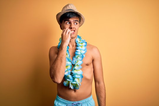 Young handsome tourist man on vacation wearing swimwear and hawaiian lei flowers looking stressed and nervous with hands on mouth biting nails. Anxiety problem.