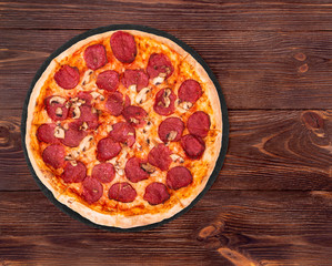 Salami pizza with mushrooms on slate bottom, on wooden table top view, space for text