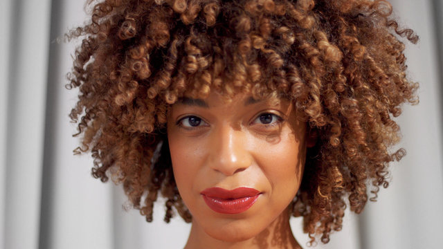 Mixed race black woman with curly hair and natural warm make-up for dark skin watching to the camera Cyrly hair texture