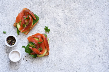 Crispy toast with avocado and salmon on a concrete background.