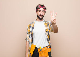 young housekeeper man smiling and looking friendly, showing number three or third with hand...