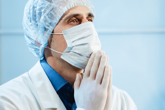 A Male Doctor Prays To The Hospital For The Patient’s Life And The End Of The Coronavirus Pandemic.