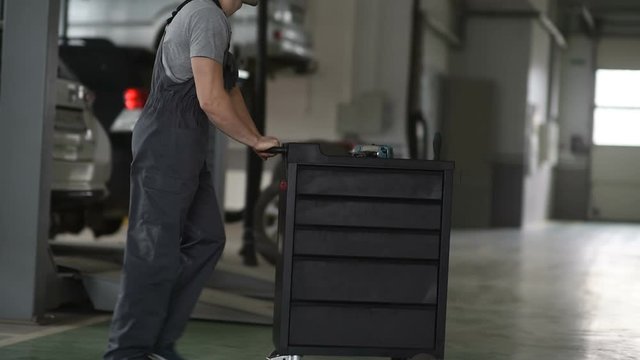 A young automaker pushes a box of tools in the workshop.