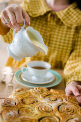 Woman pouring milk into cup with aromatic tea on table. Synabons are on the table. Tea time